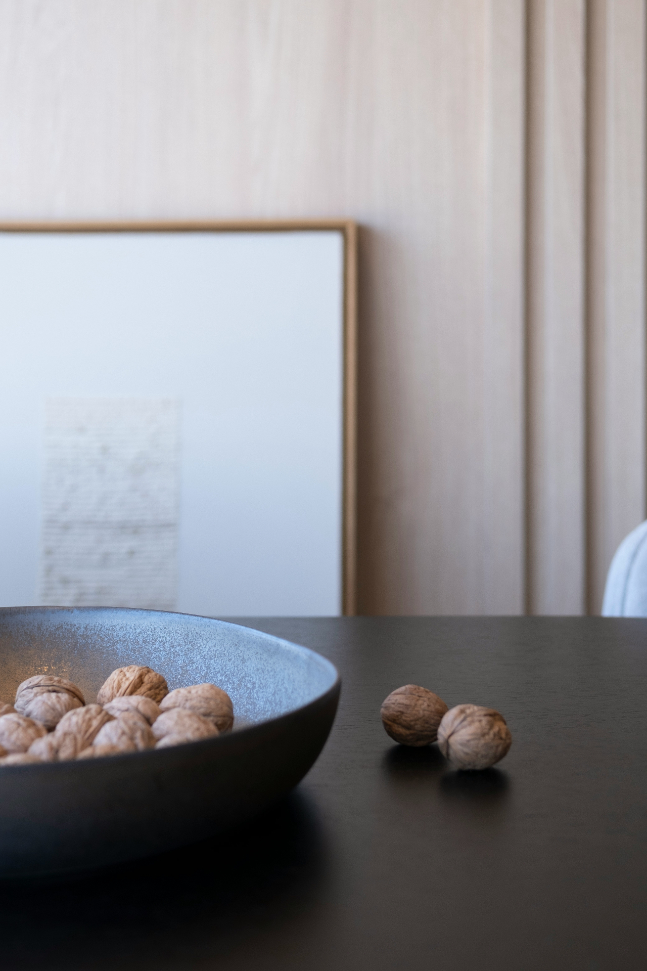 A ceramic bowl of walnuts on a dark table against a soft neutral wall